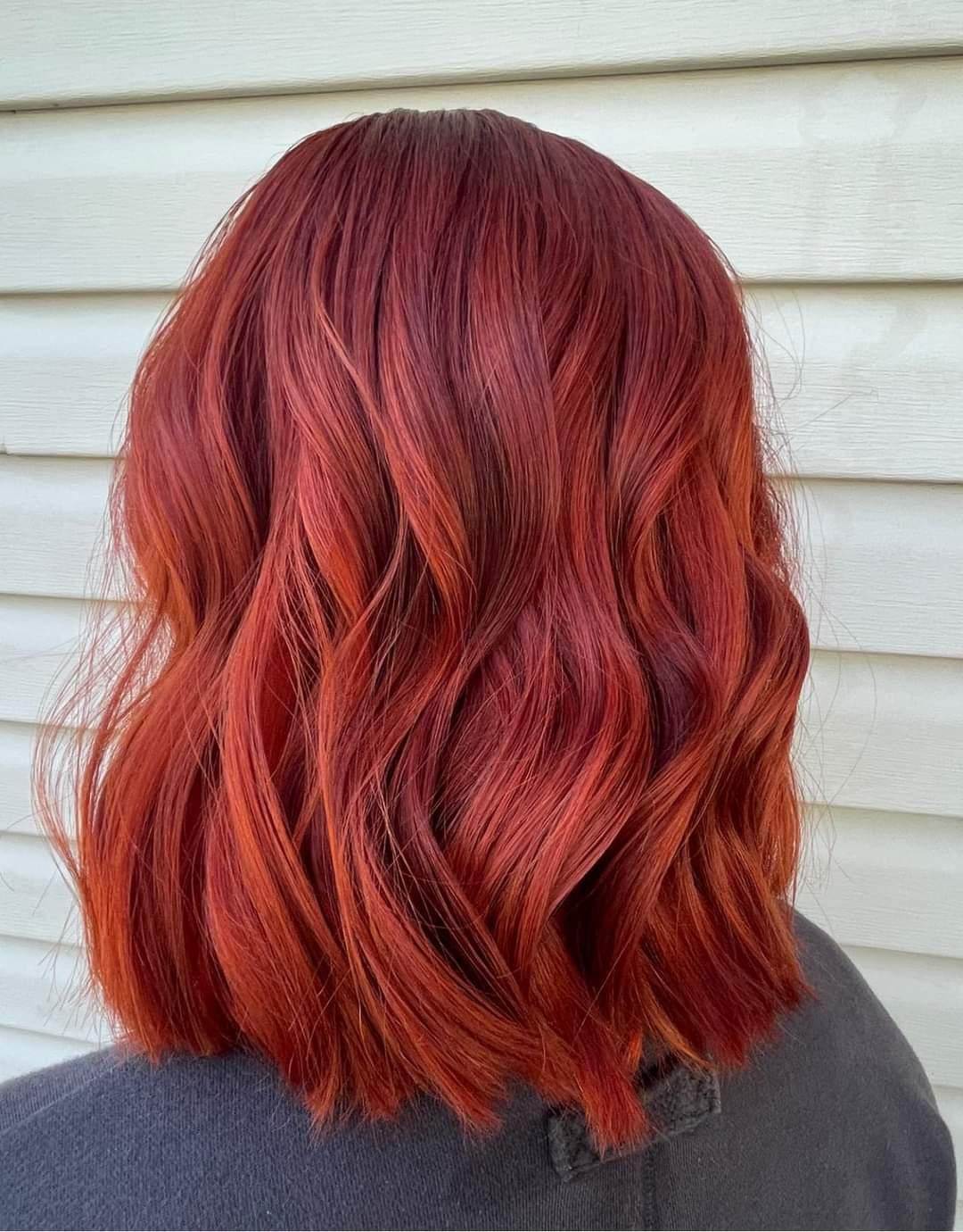 Shoulder length hair in a vivid copper red, waved.